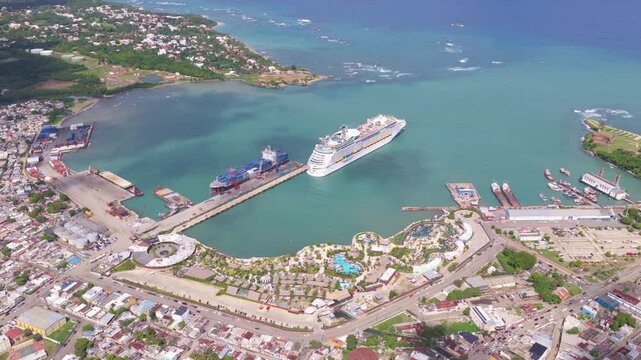 Aerial drone view of Taino Bay cruise port in Puerto Plata, Dominican Republic, with large cruise ship docked in turquoise Caribbean waters near tropical coastal city. Top down.