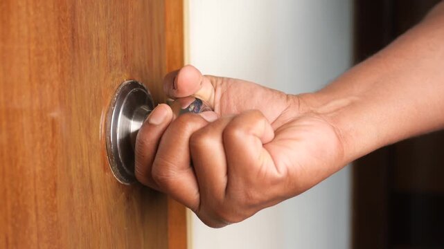 Person hand grabbing and turning silver round door knob to open wooden entry in bright room