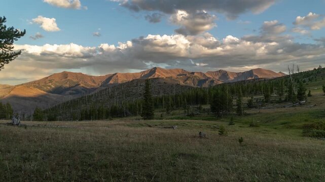 Sunset light glowing on a mountain range above a meadow as colorful clouds pass and fade into night, Absaroka Range, Montana, time lapse