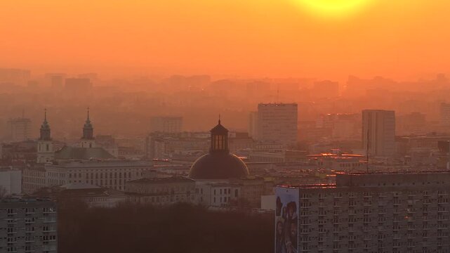 Hazy aerial cityscape of warsaw, poland, during a stunning orange sunrise. The holy trinity lutheran church dome is a prominent landmark