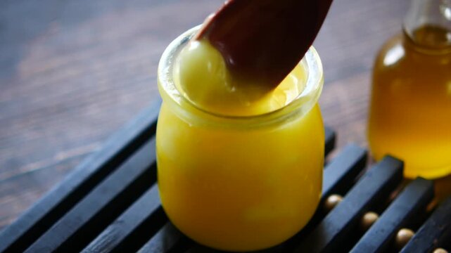 Close up of wooden spoon scooping homemade clarified butter from glass jar