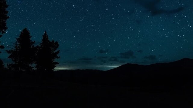 Stars and the Pleiades rising over silhouetted pine trees and a mountain ridge at a backcountry camp, Absaroka Range, Montana, time lapse