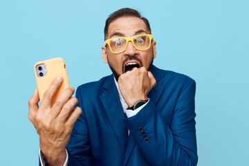 A professional businessman in a blue suit stands against a solid colored backdrop, an isolated setting, showing surprise and urgency as he checks his phone. © SHOTPRIME STUDIO