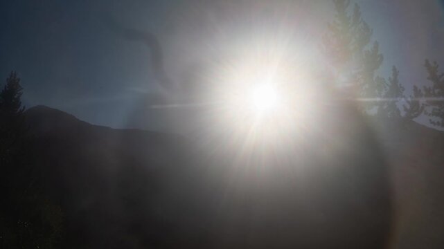 Fogged camera lens slowly clearing to reveal a glowing sun, trees and mountains, abstract time lapse
