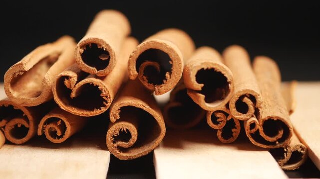 Cinematic macro shot of dried cinnamon sticks on wooden surface against black background