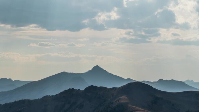 Clouds moving over hazy layered mountain silhouettes and the pointed summit of Monument Peak, Montana, time lapse