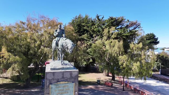 Aerial circling the equestrian bronze statue of General Manuel Bulnes in Punta Arenas, Chile, featuring the large stone pedestal and lush greenery of the city&rsquo;s historic avenue