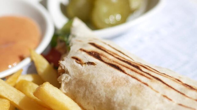 Close up of delicious chicken shawarma wrap with french fries and dipping sauce on plate in bright sunlight