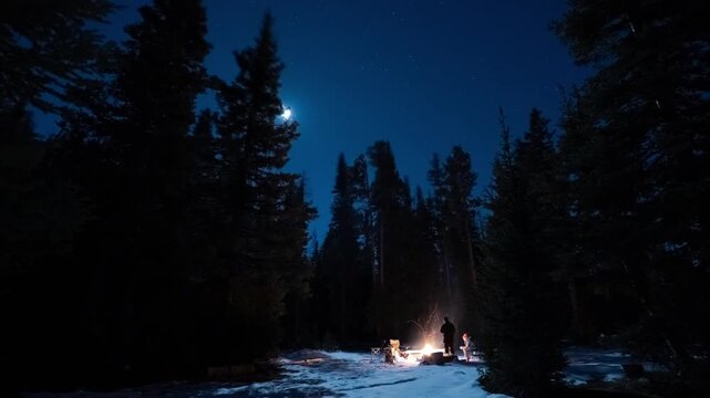 Full moon arcing across the night sky above tall pine trees and a snowy forest campsite, Gravelly Range, Montana, time lapse