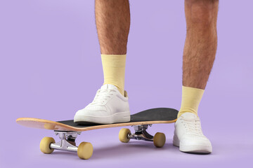 Legs of young man with skateboard on lilac background, closeup © Pixel-Shot