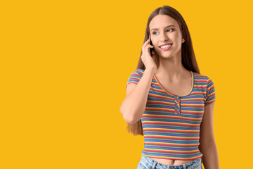 Beautiful young woman talking by modern mobile phone on yellow background