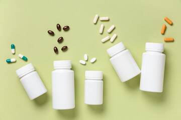 Fototapeta premium Blank plastic vitamin bottles and different pills on green background