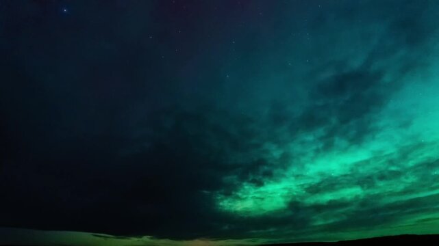 Green northern lights glowing through moving clouds over flat open plains at night, Montana, time lapse