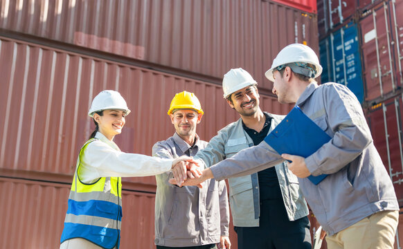 Diverse logistics team stacking hands together in container terminal at port, Professional shipping workers celebrating success with team hand stack at shipyard