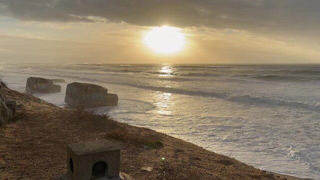 4K static shot of historical World War II bunkers on the beach of Labenne at sunset. Intense Atlantic Ocean waves crash against the concrete ruins under a dramatic, moody, overcast sky in Landes, Fran