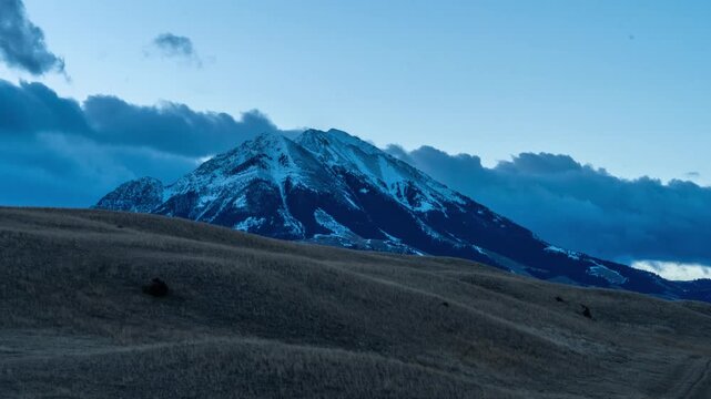 Clouds moving past snow covered Emigrant Peak at sunset above dark rolling hills, Paradise Valley, Montana, time lapse