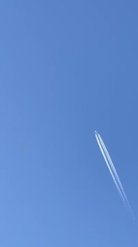 A large passenger aircraft with four engines is flying high in a clear blue sky. Commercial airliner in flight with vapor trails. Civil aviation, air travel concept.