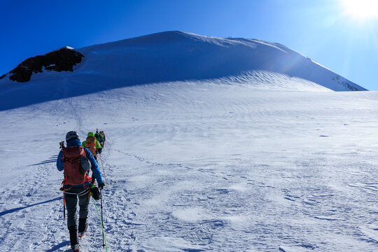 Mountaineers in rope team with crampons ascending towards mountain summit Parrotspitze and glacier panorama in the morning in Pennine Alps, Italy