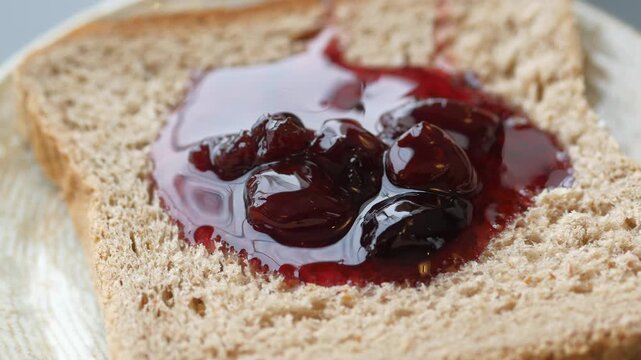 Slow motion video of cherry jam with whole fruit pieces dripping onto slice of whole wheat toast