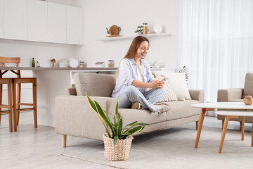 Beautiful young woman sitting on sofa and using mobile phone in living room
