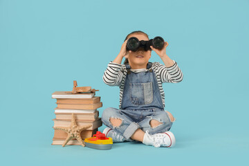 Naklejka premium Cute little girl with adventure books looking through binoculars on blue background