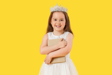 Naklejka premium Cute little girl in tiara with adventure book on yellow background
