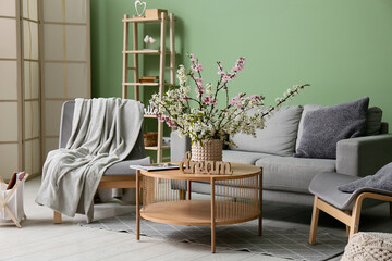 Fototapeta premium Sofa with armchairs, coffee table and vase of blooming branches near green wall in living room