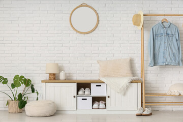 Bench and rack with clothes near white brick wall in interior of hallway