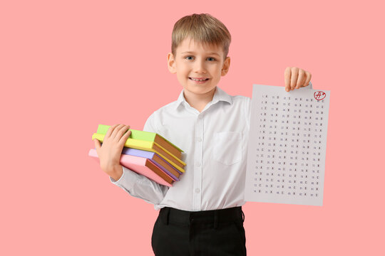 Happy schoolboy with good results of school test and books on pink background