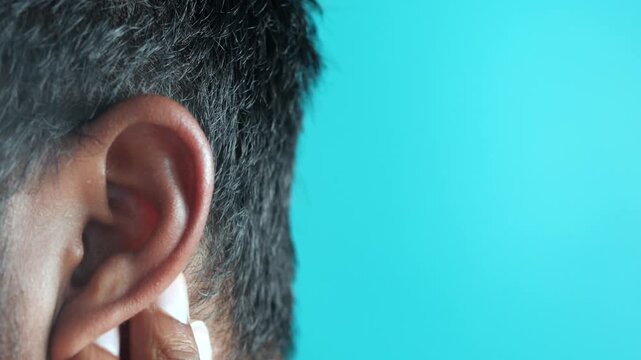 A man&rsquo;s hand rubs his ear, close up shot with a turquoise background, motion in focus