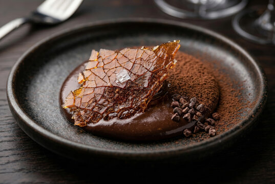 A high-detail, close-up photograph of a decadent dark chocolate dessert served on a dark matte ceramic plate.