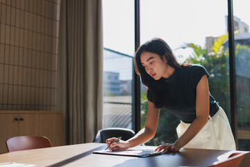 Young asian woman writing on clipboard in office