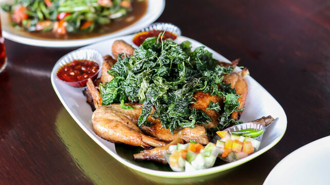 Authentic Indonesian Acehnese fried chicken (Ayam Tangkap) topped with a generous amount of crispy deep-fried curry leaves, served with spicy sambal dipping sauces and fresh vegetable garnish