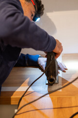 Man wearing headlamp uses jigsaw to cut a marked line on plywood during a home renovation, focused on precision and detail while working indoors on a diy carpentry project