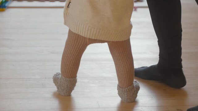 Baby takes first steps on wooden floor. Heartwarming moment perfect for family and parenting projects.