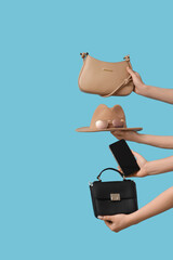 Fototapeta premium Female hands holding stylish women's bags, hat, sunglasses and mobile phone on blue background