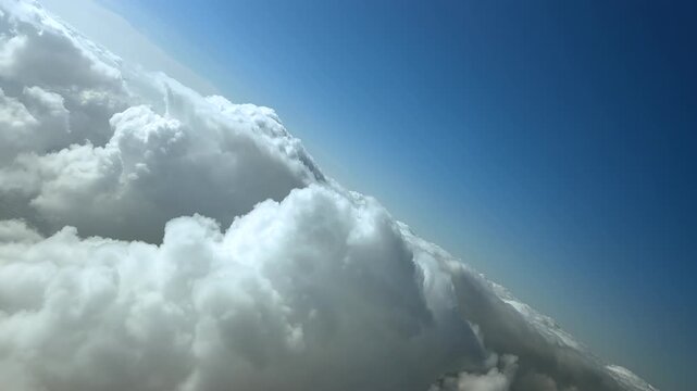 An immersive pilot&rsquo;s perspective from a jet cockpit flying in an abrupt left turn over the tops of cottony clouds under a blue sky.