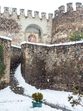 Ancient stone staircase and massive fortress walls of Rabati Castle in Akhaltsikhe, Georgia, covered with white snow during winter season, featuring medieval architecture and a stone archway.