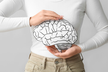 Young woman with paper brain on grey background, closeup. Brain Injury Awareness Month