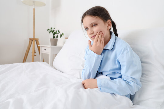 Cute girl suffering from toothache in bedroom