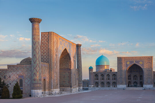 Ulugbek and Tillya Kari madrasa with turquoise dome at sunrise in gentle golden-pink rays of sun, clear blue sky. Ornate facade of timurid islamic architecture landmark Registan square, Uzbekistan.