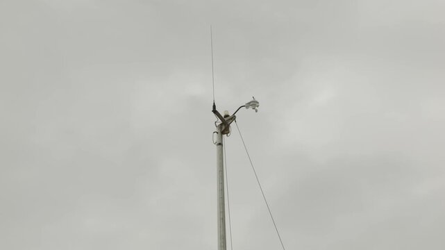 Sail boat mast with weather vein spinning against grey sky stock footage