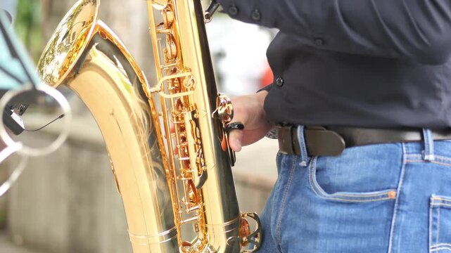 Musician adjusts golden saxophone ready to play music outdoors on street