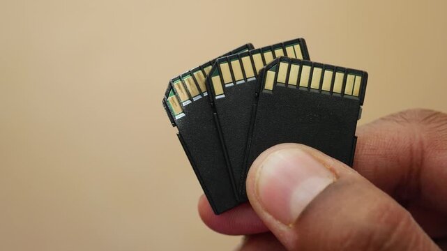 Person holding three secure digital memory cards showing golden pins on beige background