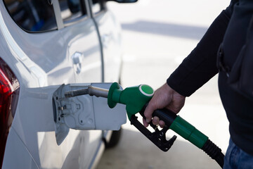 man refilling car with gasoline at gas station, hand holding green fuel nozzle close up, white vehicle parked outdoors, concept of oil industry, energy sector, fuel economy, automotive services © Lana Pietukhova