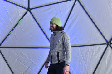 Man with long curly hair wearing a green beanie inside a geodesic dome © salajean