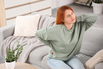 Beautiful young woman suffering from back pain on sofa at home