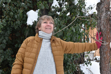 Woman in mustard puffer jacket leaning against a tree in the snow © salajean