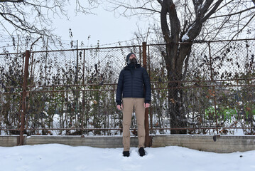 Man in black puffer jacket and tan pants standing in the snow © salajean