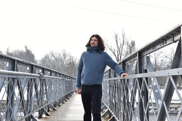 Man with long curly hair walking on a metal bridge wearing a blue fleece pullover in winter © salajean